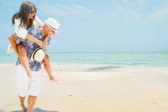 Carefree young man woman piggyback ride walking along turquoise ocean sand beach global tropical island resort destination sunny summer honeymoon getaway