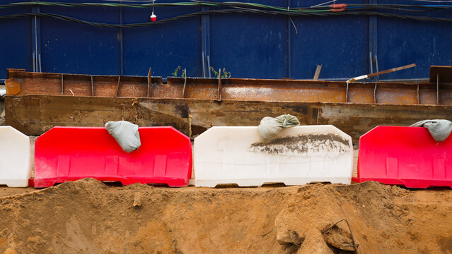 Red and white temporary barriers secured with sandbags around an active excavation area, representing construction safety, restricted access and work zone protection