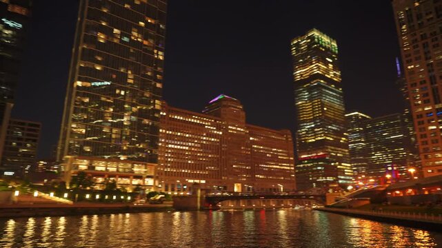Illuminated skyscrapers and colorful office buildings reflect across the Chicago River at night in downtown Chicago. Modern waterfront architecture and glowing city lights create a vibrant urban