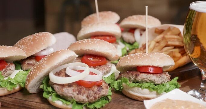 Burgers, onion and cheese in a close-up of grilled meat patties, tomato slices and lettuce inside sesame buns on a wooden board, with creamy dipping sauce and fries for pub dining and menus.