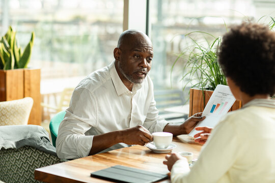 Man presenting bar chart to colleague at cafe