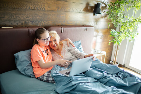 Grandmother and granddaughter using laptop in bed at home