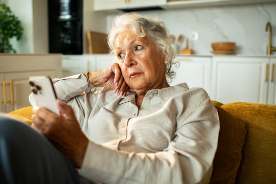 Senior woman looking away while holding smartphone at home