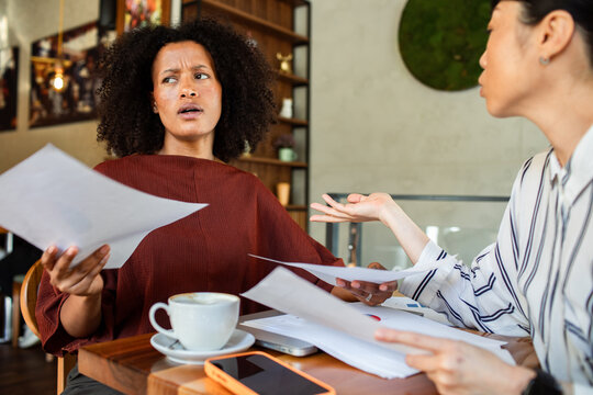 Two women discussing confusing paperwork at a cafe table