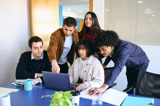 Diverse Group of young latin professionals engaged in a discussion at an office, hispanic teamwork using laptop at workplace
