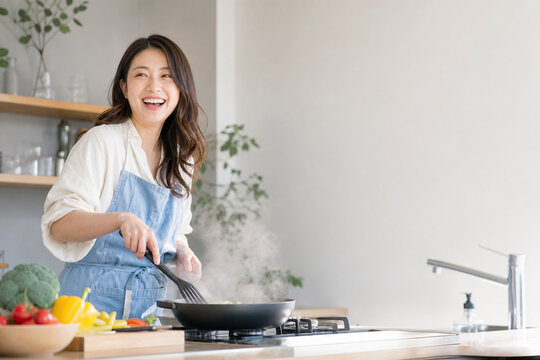 キッチンでフライパンを使って調理する日本人女性