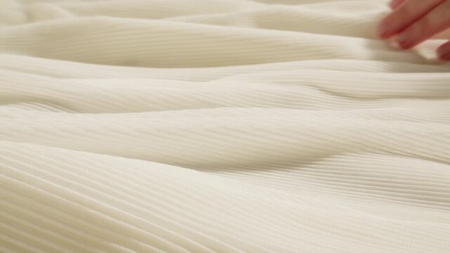Ribbed fabric texture in cream color, close up of soft pleated knit textile with hand touching, beige knitted cloth background for fashion design and interior upholstery