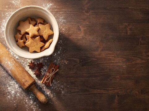 Top view of star-shaped gingerbread cookies in ceramic bowl with rolling pin and spices on dark wood, rustic Christmas baking background concept