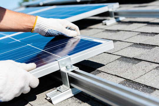 A construction worker wearing gloves installs solar panels onto a residential roof structure.