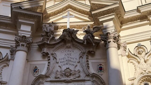 Baroque church facade detail with a cross, sculpted angels and a Latin inscription cartouche, Rome, Italy