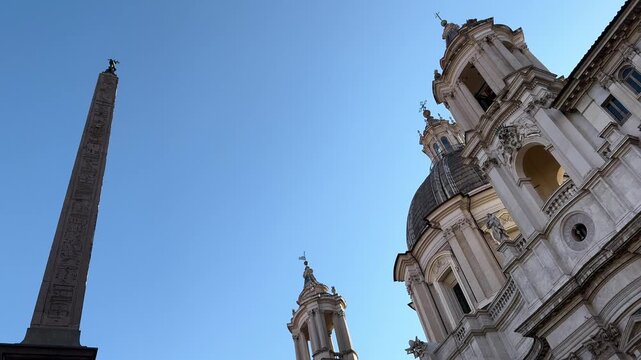 Dome and bell towers of Sant'Agnese in Agone rising above a marble statue against blue sky, Piazza Navona, Rome, Italy