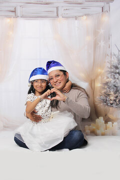 Divorced single mother and her 5-year-old Latina daughter with glasses excited celebrate Christmas and New Year's together, wearing Santa hats