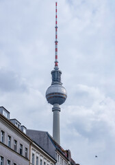 Vertical view of the Berlin TV Tower from Almstadtstraße in Berlin-Mitte, with its sphere and antenna rising above residential rooftops against a cloudy sky. © Timothy Shoot