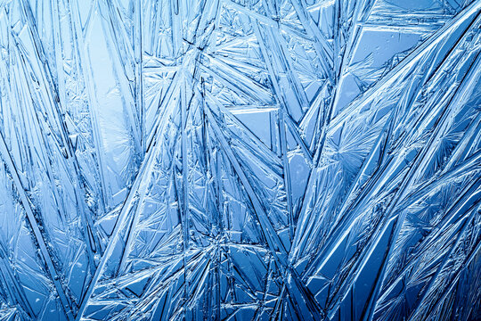 Ice frozen in intricate patterns of delicate crystals with brilliant contrasts of deep blues. Real unique patterned crystal formations. Sparkling window frost or icy cold winter frosting background.