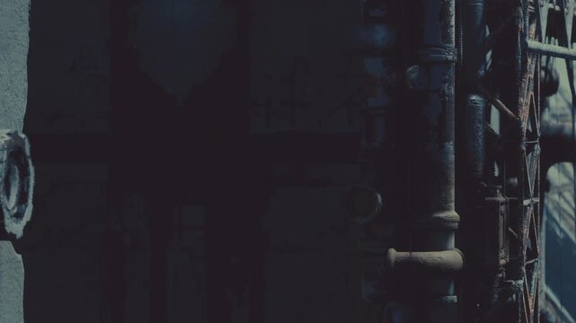 Faded textures and shadows linger in an old industrial site during dusk. The ambiance feels mysterious as rusted pipes catch glimpses of the dim light. Nature begins to reclaim its space.
