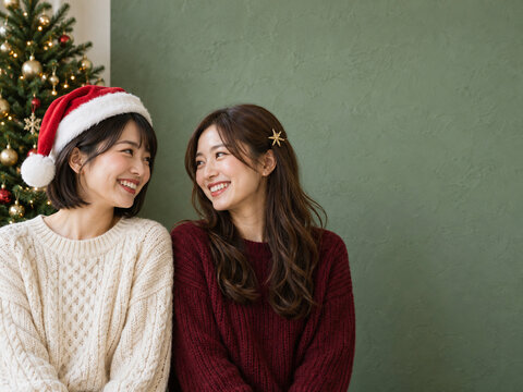 クリスマスツリーのそばで笑い合う女性二人と緑の背景