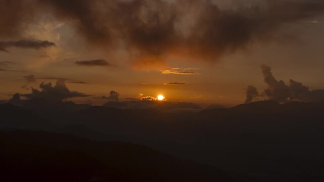 Sunset timelapse over a mountain landscape, capturing the movement of clouds across the peaks as the sky changes color in the fading evening light.