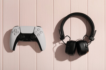 Gaming and entertainment lifestyle, modern video game controller and wireless headphones on a pastel pink wooden background for leisure and hobby © Pixel-Shot