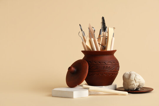 Pottery and ceramics workshop, clay sculpting tools in a rustic clay pot with raw clay on a beige background for creative hobby and craft projects