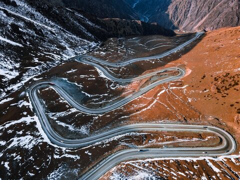 High perspective view of sharp switchback curves on asphalt mountain road across brown snowy ridges