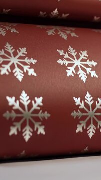 Vertical video: Panning phone revealing red wrap rolls on white table showing snowflake reflections