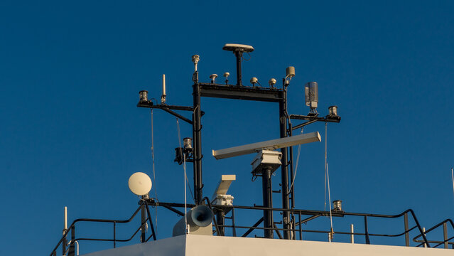 Ferry upper deck with railings, antennas, satellite dish, loudspeaker, and navigation equipment against a clear blue sky at sea