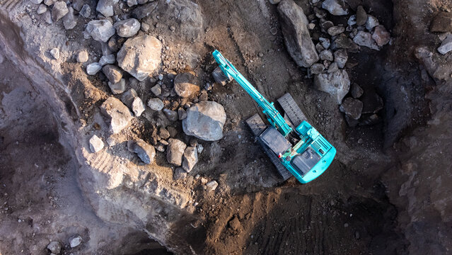 Aerial view of an excavator working in a deep dirt pit with rocky terrain and shadows cast on the ground in Indonesia
