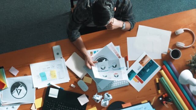 Top view of designer writing and designing logo graphic at meeting. Closeup of business man working on colored palettes and writing idea on sticky notes on table with equipment and paper. Symposium.