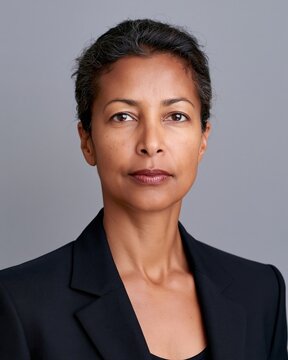 Close portrait of confident woman in black blazer against plain gray background