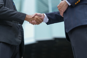 Two male executives complete a deal with a tight handshake outdoors in the green outdoor courtyard of a downtown business complex, the gesture reads clean and symbolic © ultramansk