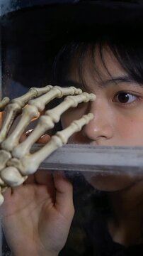 Vertical video: Moving bony hand prop, teen opening eyes and tracking finger at window wearing hat
