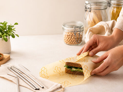 A person wraps a sandwich with a honeycomb beeswax wrap on a light countertop, demonstrating a sustainable food storage solution.