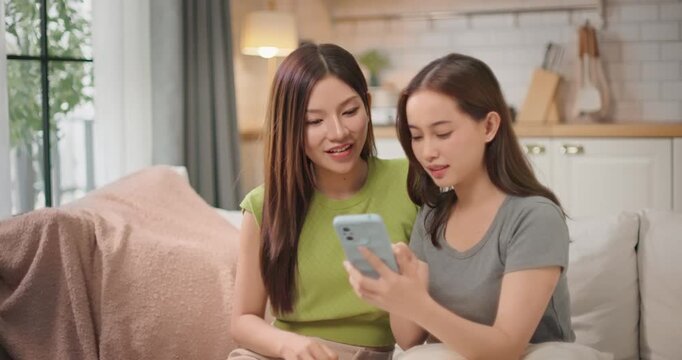 Two Asian woman friends reacting to gossip on smartphone at home. Two girls intensely focused and amused as they scroll through viral news online, fun, curious and surprise moment in casual lifestyle.