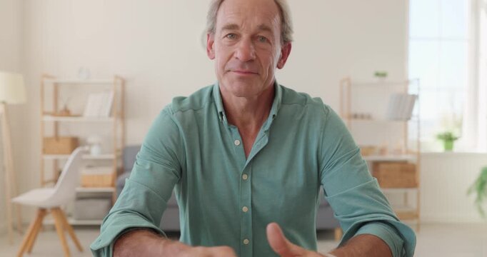 Mature man talks to camera online. Having online video call or remote conversation from home. He wears a green shirt. Daylight fills the room. Concept of online communication for seniors.
