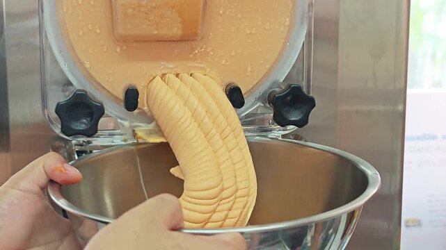 Fresh Thai tea gelato ice cream dispensing from a batch freezer machine into a bowl.