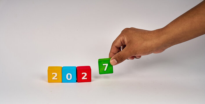 Hand placing green number seven beside colorful 2027 blocks