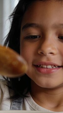 Vertical video: Sticking tongue girl in overalls offering spoon to mouth tasting in kitchen, bowl