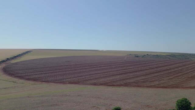 Large arable field shows freshly tilled red soil with dense parallel furrows in Sao Joao d'Alianca, Goias, Brazil, characteristic of mechanized grain farming in the Cerrado, drone forward flyover.