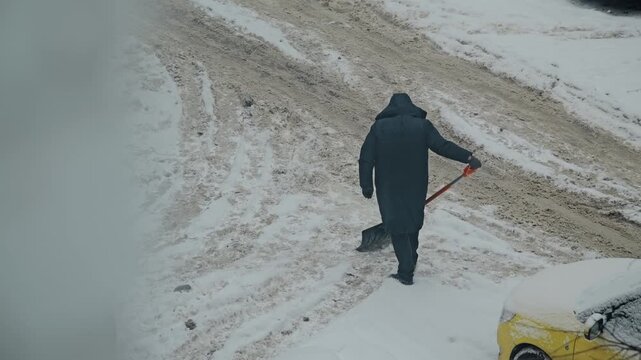 Caretaker pushes a snow shovel one handed with little snow actually removed