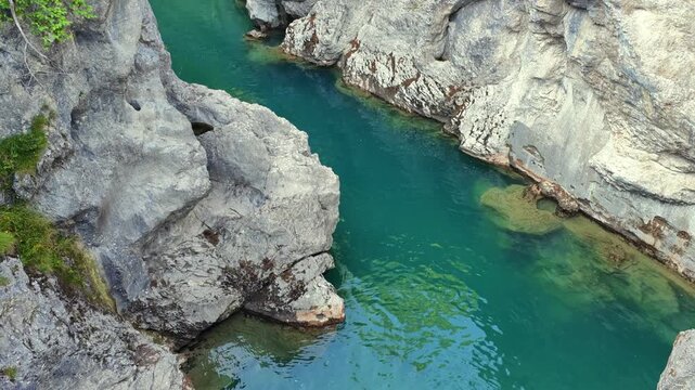 View down into the Lech gorge below the Lechfall, where clear turquoise water winds between eroded white limestone rocks and green plants in Fussen, Bavaria.
