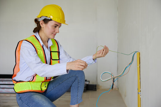 Female construction worker crouching and examining electrical wires on a construction site