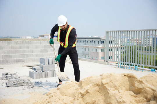 Construction worker is shoveling sand on a sunny day. He is in the process of building something new.