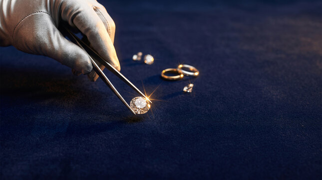 Bijoutier manipulant un diamant pr&egrave;s de bagues sur un tissu sombre