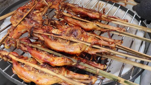 Perfectly roasted whole chicken in bamboo sticks being turned by a street food vendor, Thai street food