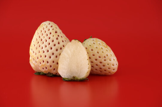 Unique white pineberry strawberries, one sliced in half, displayed on a vibrant red background