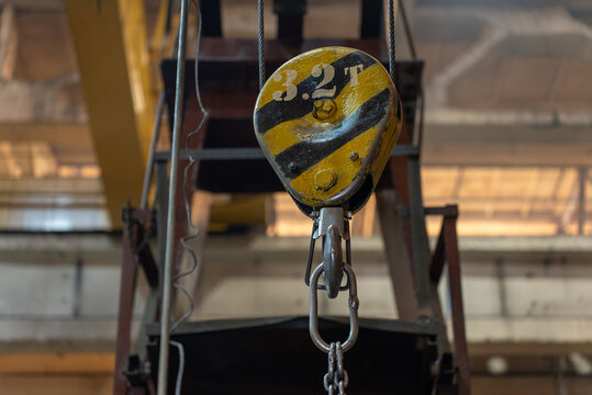 Yellow and black overhead crane hook block marked 3.2T with lifting chain in factory workshop
