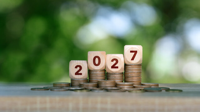 2027 Wooden number blocks and stacks of coins with green bokeh background for financial planning, savings growth and investment goals. green investment and New Year Resolution concept.