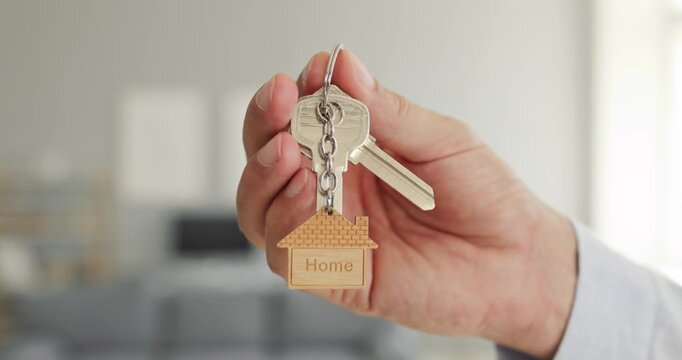 Hand holds keys for home buying. Person displays a keyring and wooden house token indoors for mortgage, property sales, rental listings, and moving. A practical real estate concept.