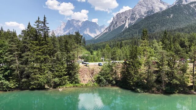 Weissensee emerald lake sits below dramatic alps peaks near Biberwier, Austria, aerial drone pulls back over forest and mountain valley.