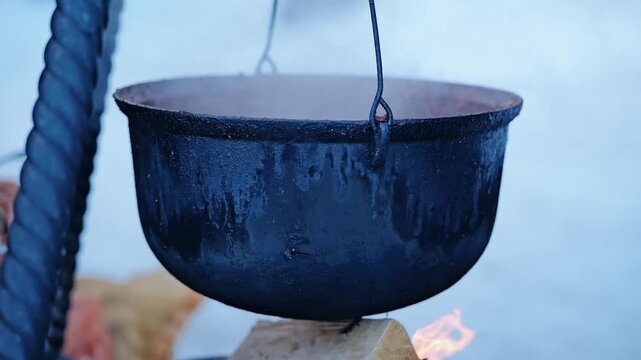 Traditional black pot hangs above open flames while steaming outdoors in winter